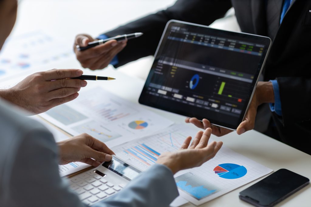 Business colleagues review charts and dashboards on a tablet during a meeting, with pens pointing at the data.