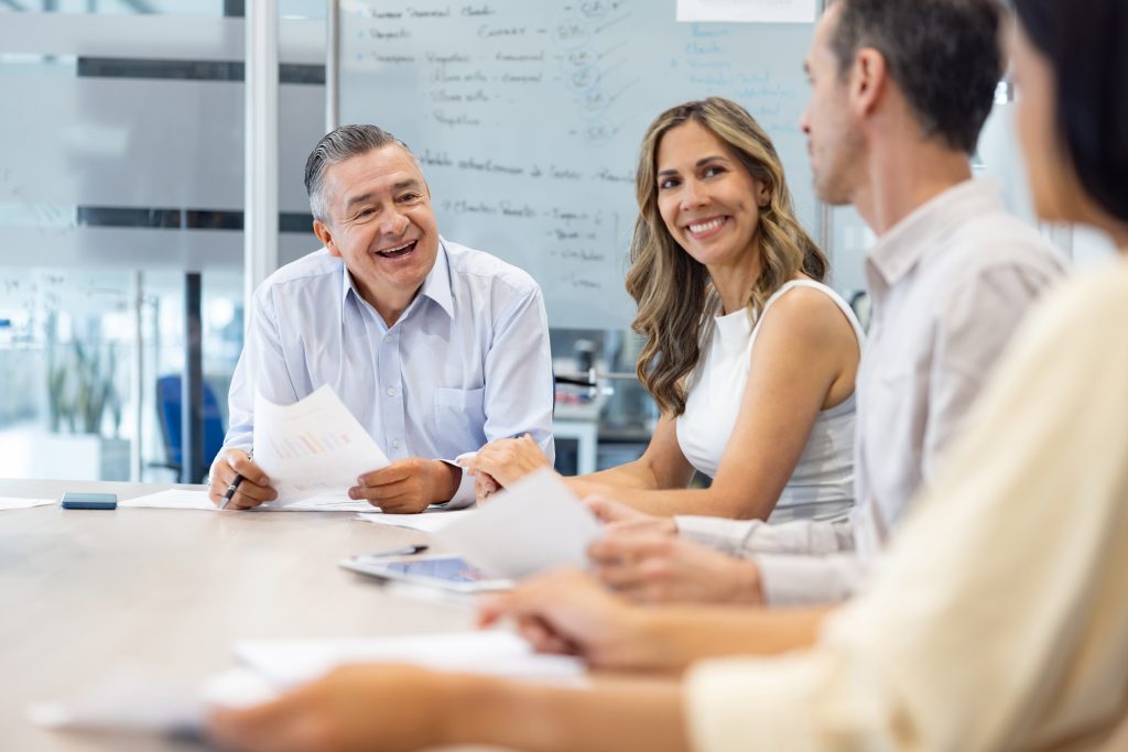 Group of four professionals seated at a conference table, examining documents and smiling during a meeting.