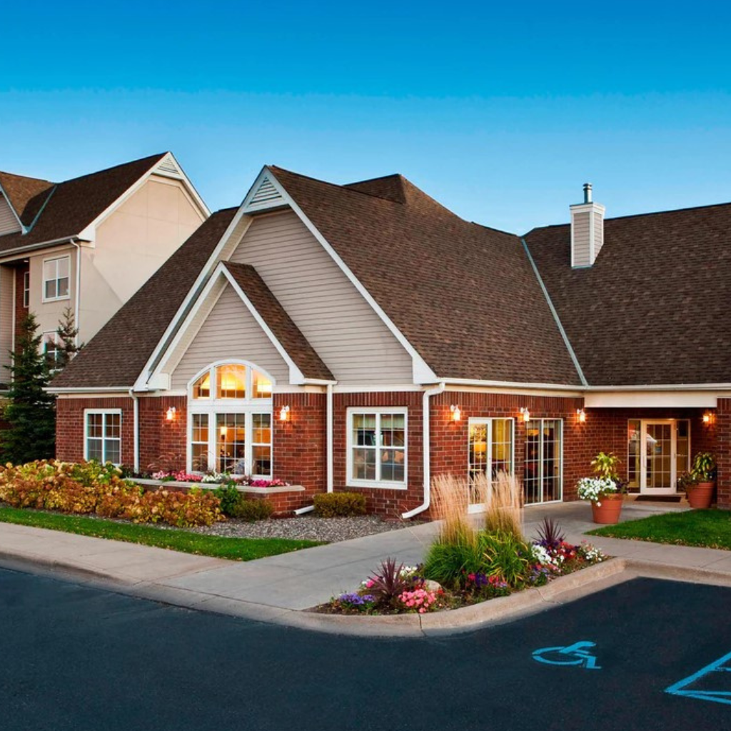 Brick residential building with a brick facade, gabled roof, and a landscaped entrance; a handicap parking space is visible in the foreground.
