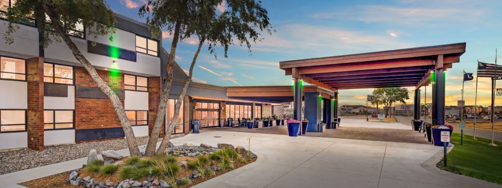 Modern office building with a wide covered drop-off area, planters, and a sunset sky.